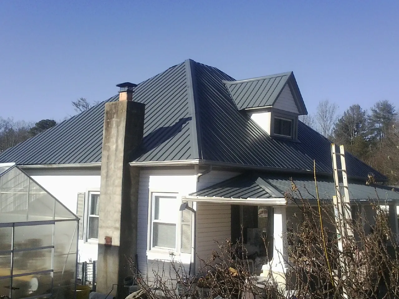 Dark blue standing seam metal roof on a white farmhouse with dormer — Slate & Tile Roof Repair by Roofing Brothers in Lavon