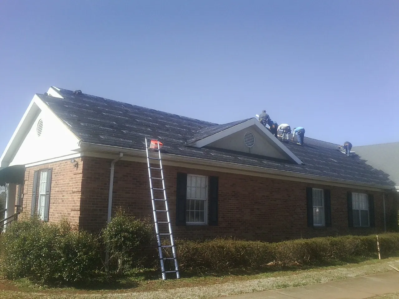 Crew tearing shingles off a brick ranch roof with a ladder set — Emergency Roof Repair work by our crew in Lavon