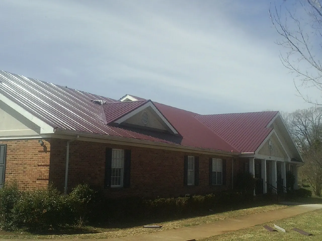 Red metal roof with gabled entries on a long brick building, from a Hail Damage Roof Repair job in Lavon