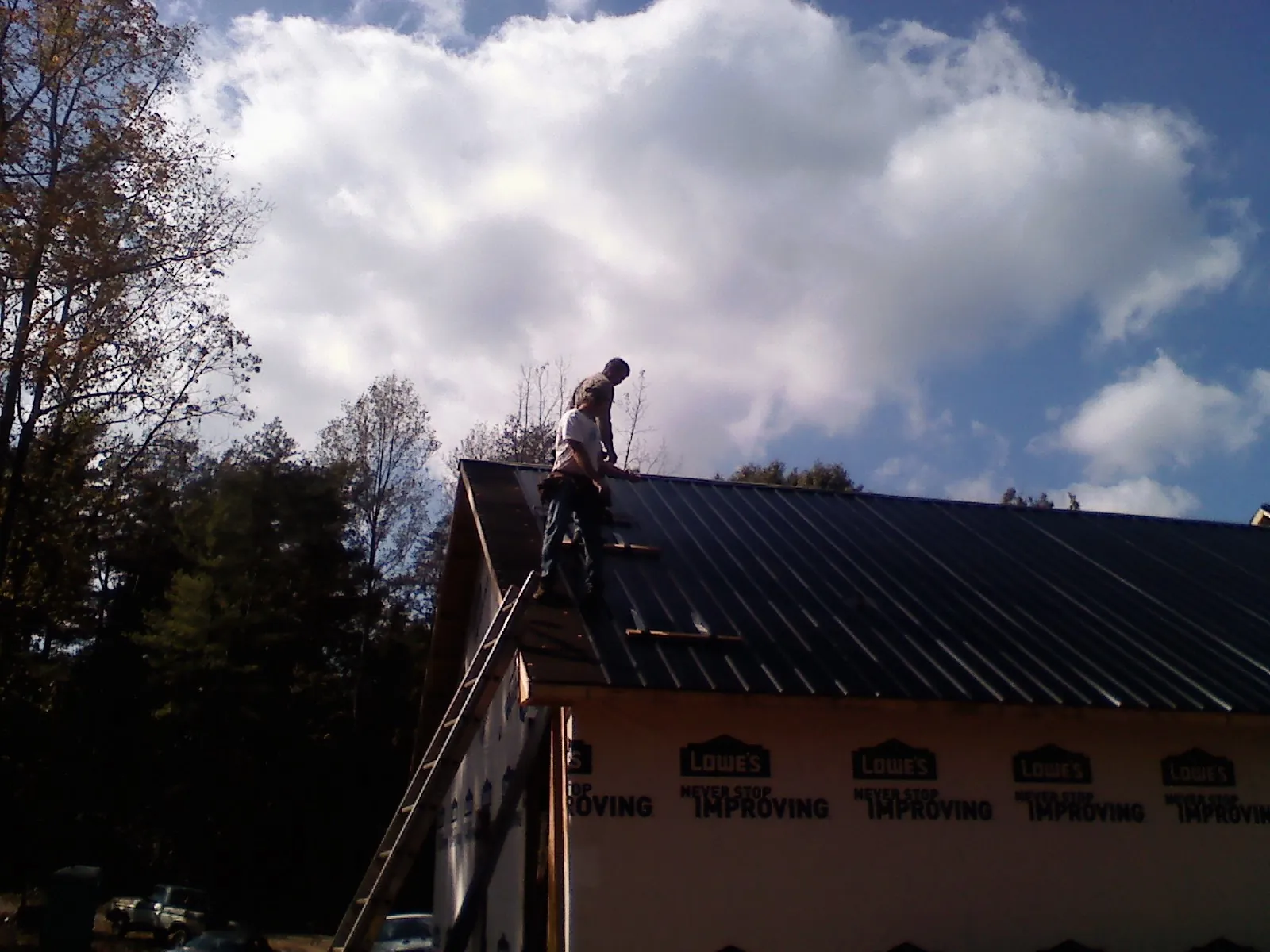 Roofer fastening dark metal panels high against a cloudy sky, from a Roof Inspection job in Lavon