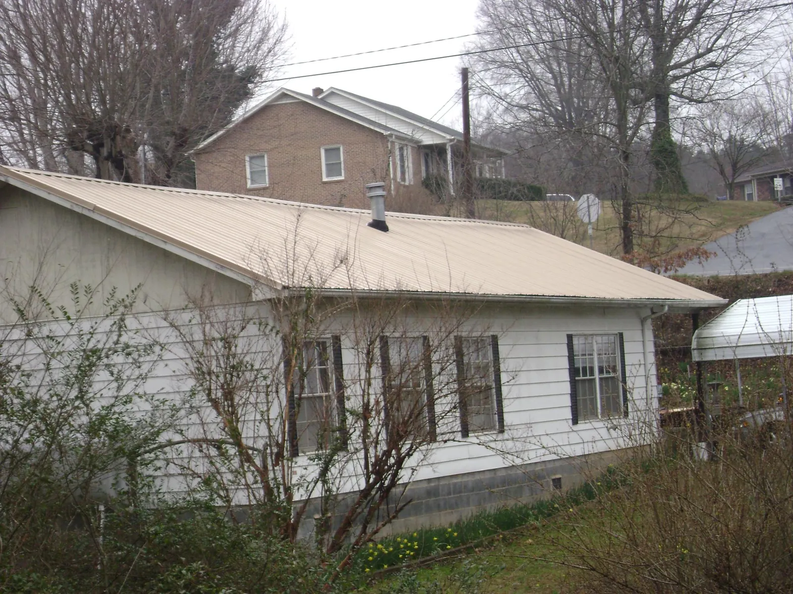 Tan metal roof on a white sided house set into a hillside — Commercial Roofing by Roofing Brothers in Lavon