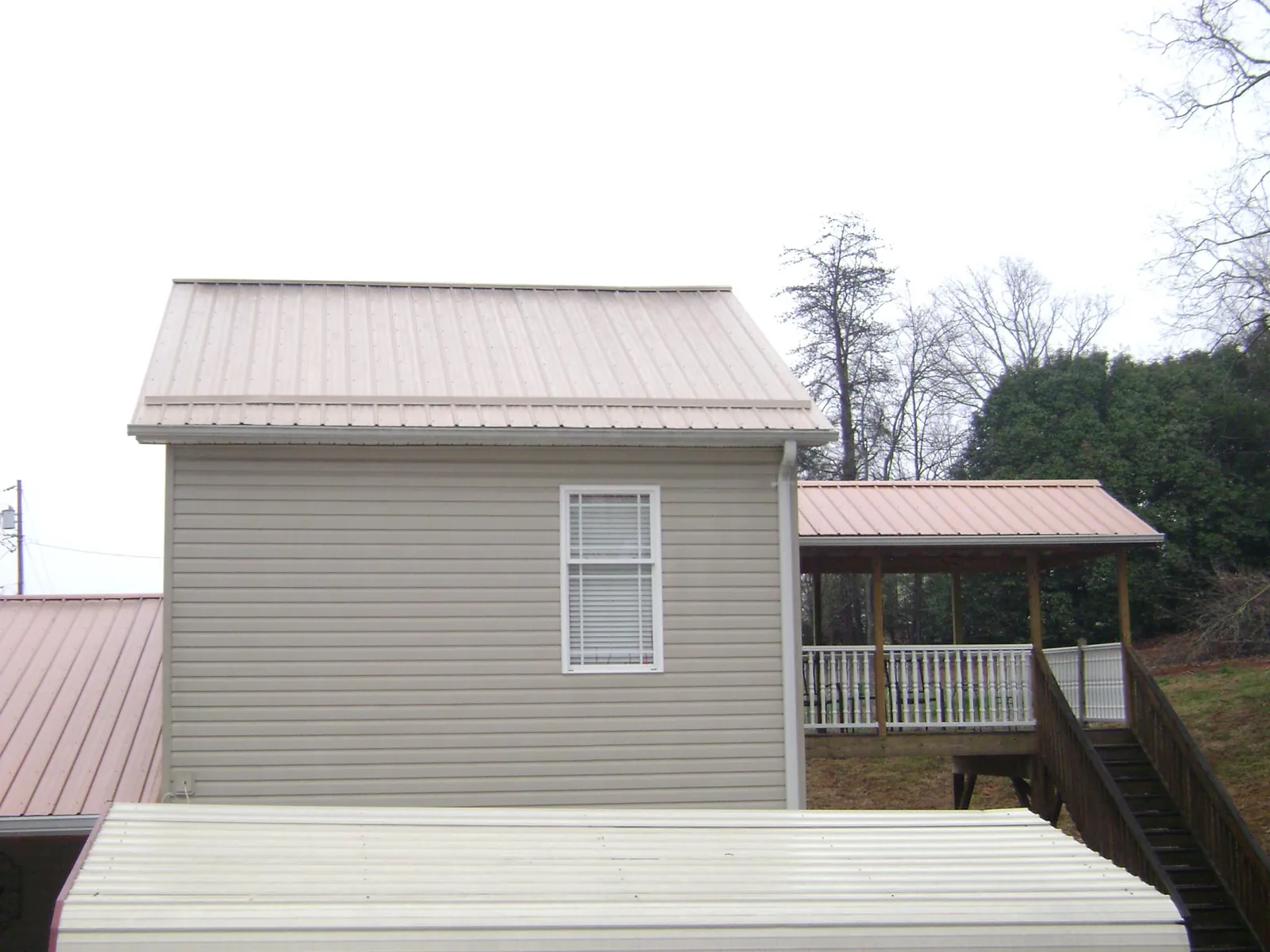 Tan metal roofs on a two story addition and attached porch, from a Roof Replacement job in Lavon